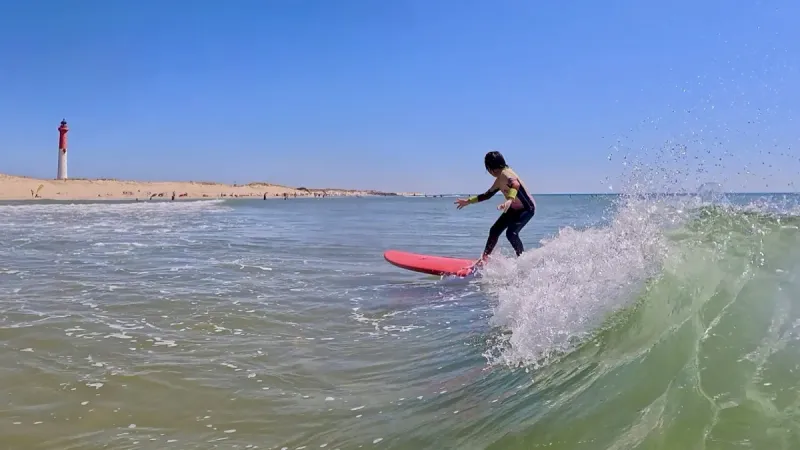 Surfeuse sur une vague avec vue sur le phare